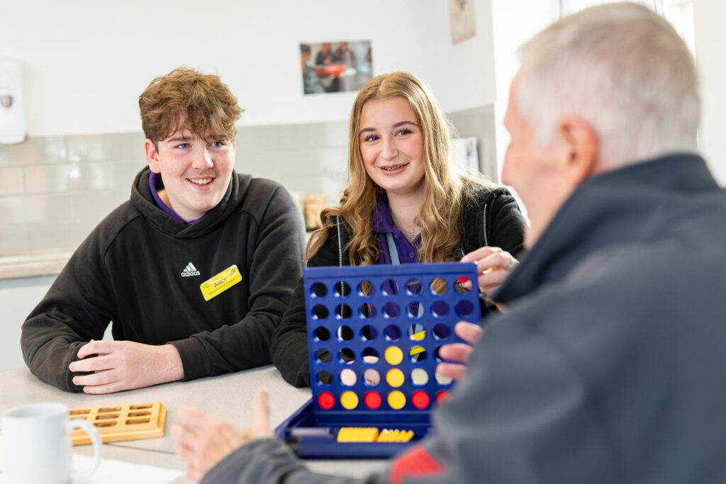 two students playing a game with an elderly gentleman